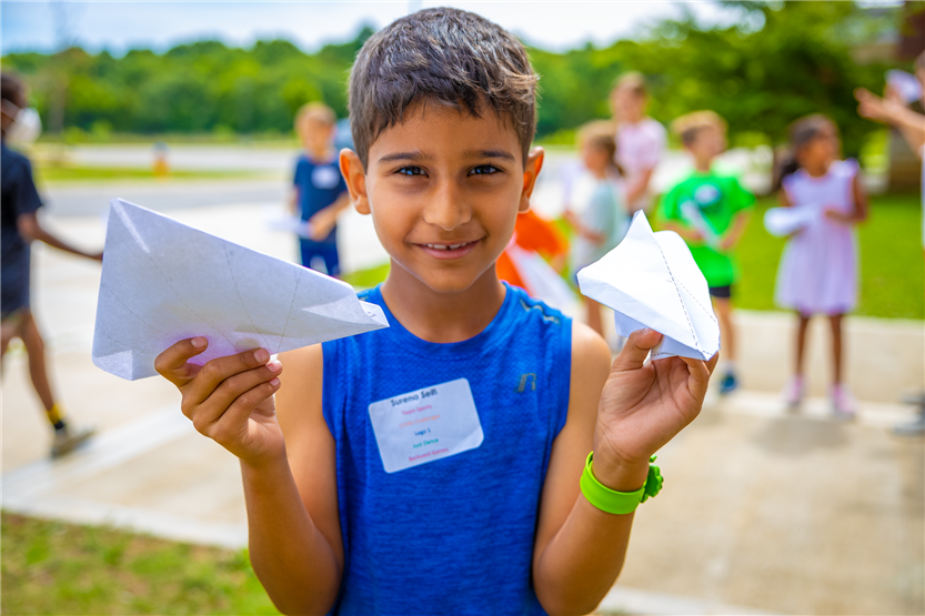 A boy wearing a blue shirt holds up two paper airplanes